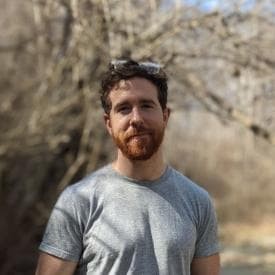 Photo of James O'Beirne in a dry field, from the front, wearing a gray flannel.